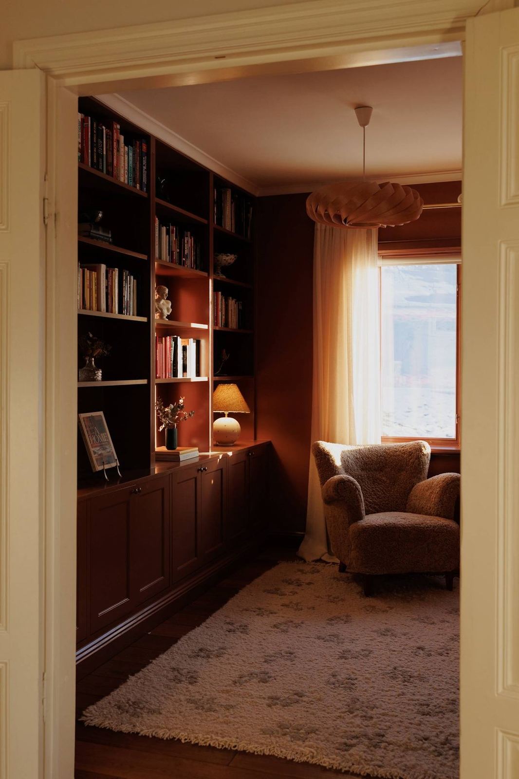 The library seen through the doorway, with sheepskin armchair and window light
