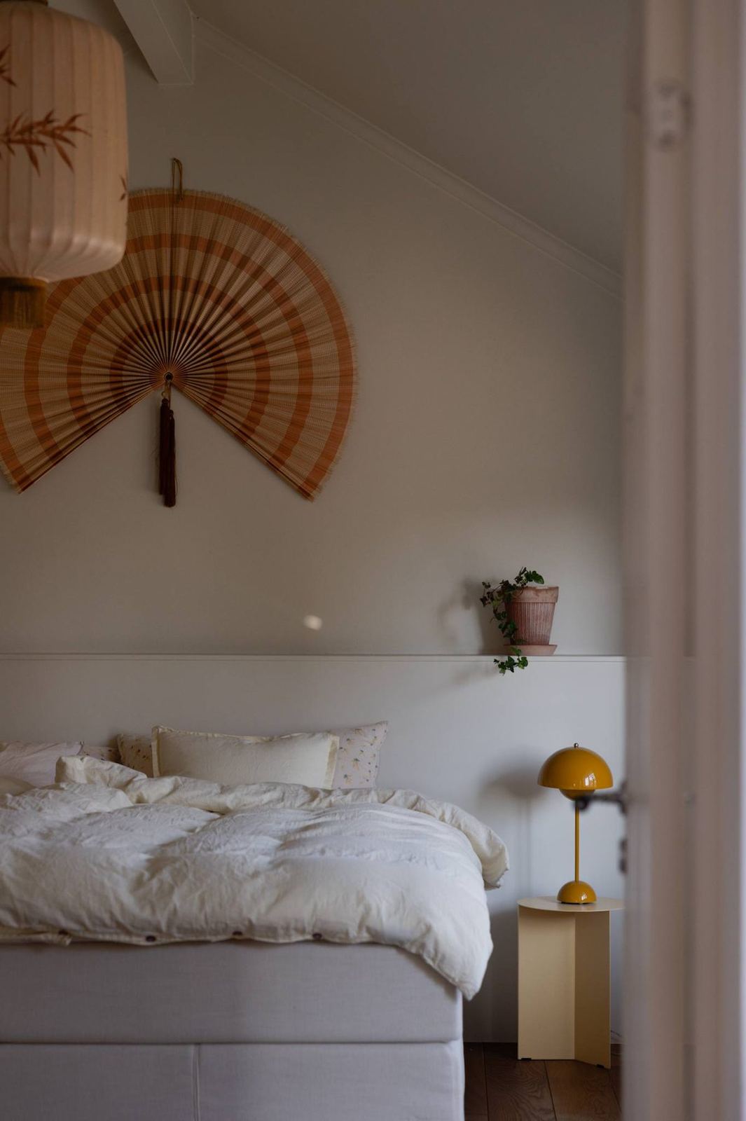 Master bedroom with cream linen, a paper fan and a yellow lamp