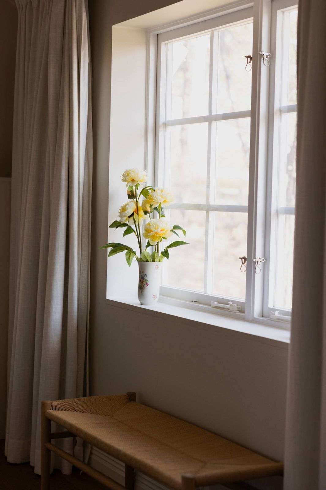 Woven bench by the window with peonies in the master bedroom