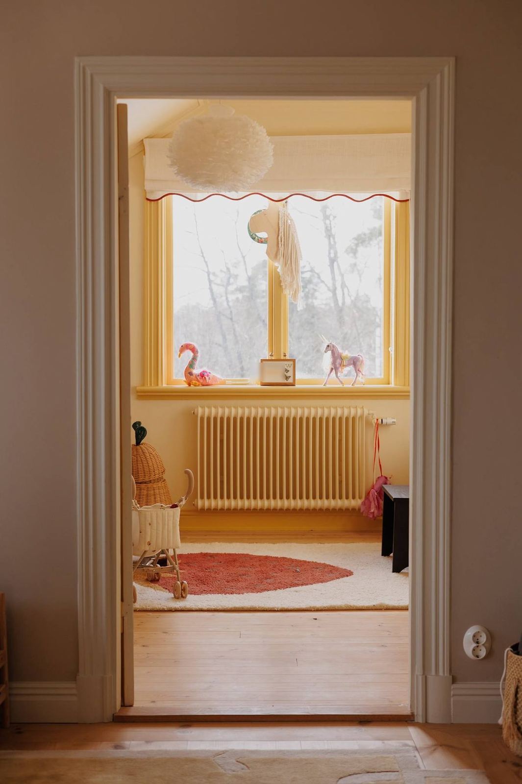 A child's yellow room seen through the doorway, with feather pendant light and strawberry rug
